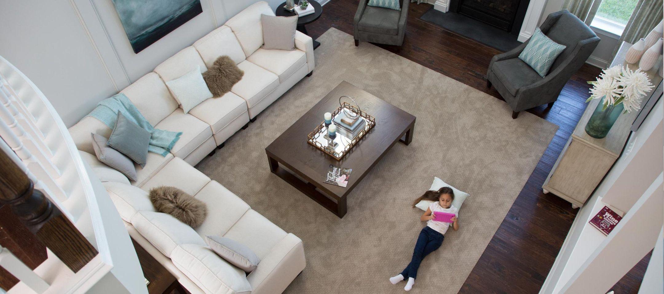 View of a living room from above with a young girl laying on the rug reading a book with her head on a pillow.